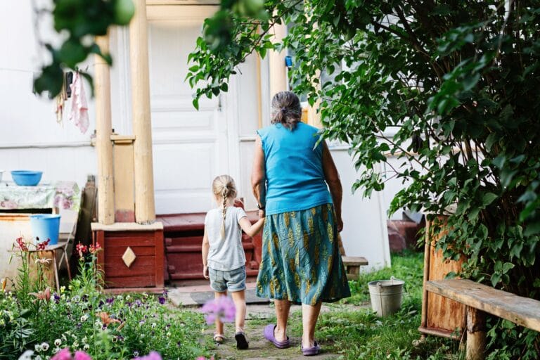 Child holding grandma's hand walking towards house